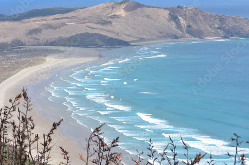 Sandy beach washed by oceanic surf with hills in background at Cape Reinga where Tasman Sea meets Pacific Ocean.