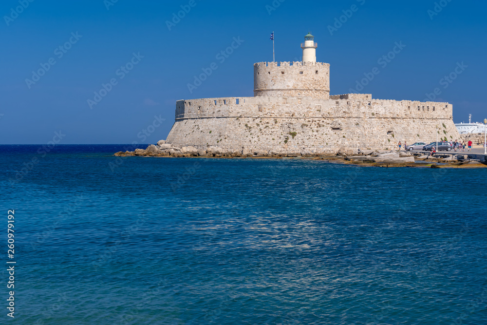 Rhodos, Greece - August 2016: Fort of Saint Nicholas at the entrance in the Mandraki old harbour of the City of Rhodes. Stone fortress or castle on the seashore against a clear blue sky and water.
