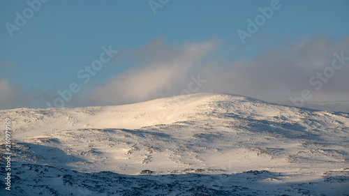 Calm Swedish Lapland winter landscape in Stora Sjöfallets Nationalpark with snow covered rolling hills during sunrise, view clouds, light sky, view from Vakkotavare to Stuotakjaure