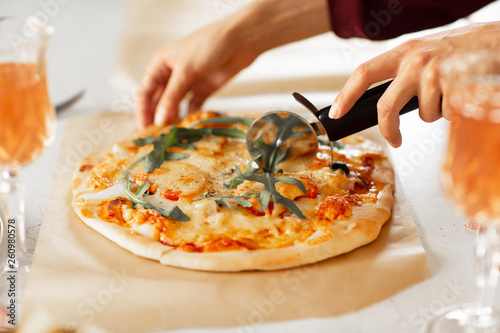 Woman's hand with a knife cut the pizza on white background close-up
