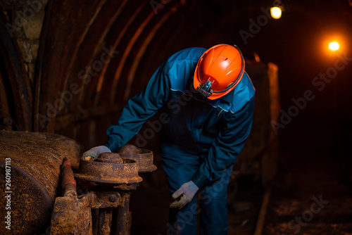 An elderly man dressed in work overalls and a helmet stands near the old inverted vogonetki. Mine worker. Miner