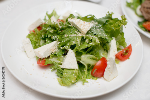 Plate of green salad with vegetables, goat, cheese tomato. Top view, horizontal.