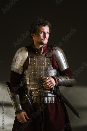 Medieval man knight in armor and weapon on dark background. Portrait of the knight