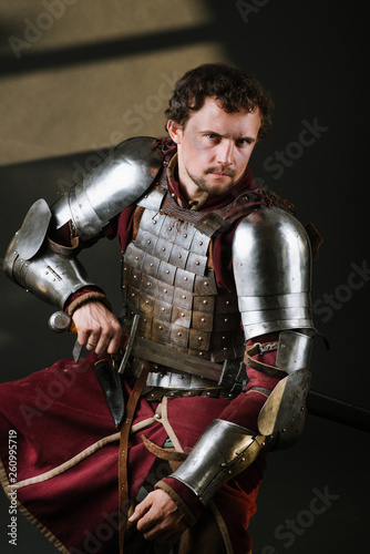 Medieval man knight in armor and weapon on dark background. Portrait of the knight