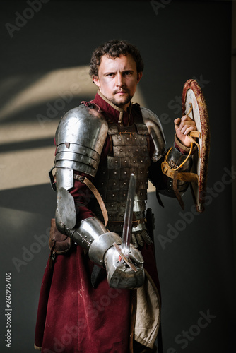 Medieval knight in armor holding sword and shield on the dark background