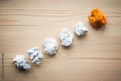 White crumpled paper balls folded in line with orange different paper ball on the top. Concept of problem solution, think different, think out of the box, leadership.