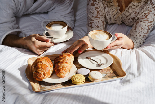 Breakfast in bed. Window light. Two cups of coffee for couple, croissants, butter and sweets