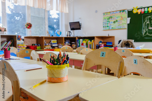 Room in elementary school, interior with light wooden furniture and learning aids on the walls. Pencils on the tables. No one, the children went for a walk