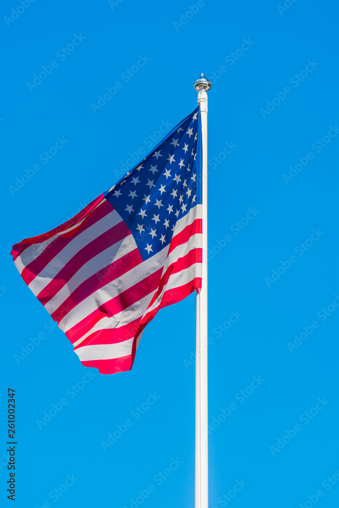 Obraz premium The flag of the United States of America sways in the wind on flagpole against a background of clear blue sky.