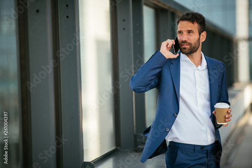 Businessman in a blue suit, talking on the phone. Manager on his phone while on coffee break. Boss having a call while drinking coffee. 