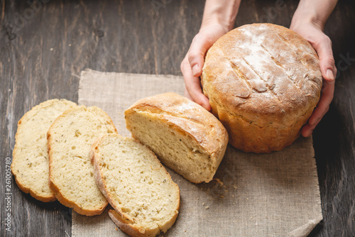 Female hands holding homemade natural fresh bread with a Golden crust on a napkin on an old wooden background