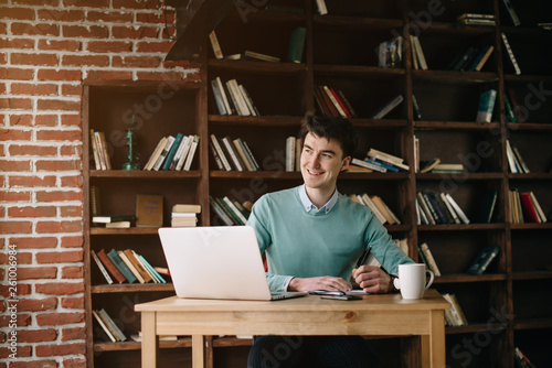 Young handsome student typing on his notebook his diploma. Student discussing on the phone universities's timetable. Education online. Work on freelance. Software development.