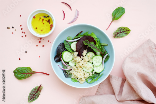 Beetroot salad with quinoa, cucumber, various lettuce leaves and onions on pastel pink background