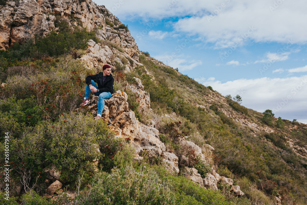 Fototapeta premium Young male sits on the rock and enjoys beautiful mountain landscape.