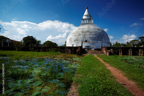 Travel destination. Buddhist Temple, Tissamaharama, Sri Lanka. Path between two ponds covered in water lilies leading to the white temple, blue sky with clouds in background. Tourist hot spot.