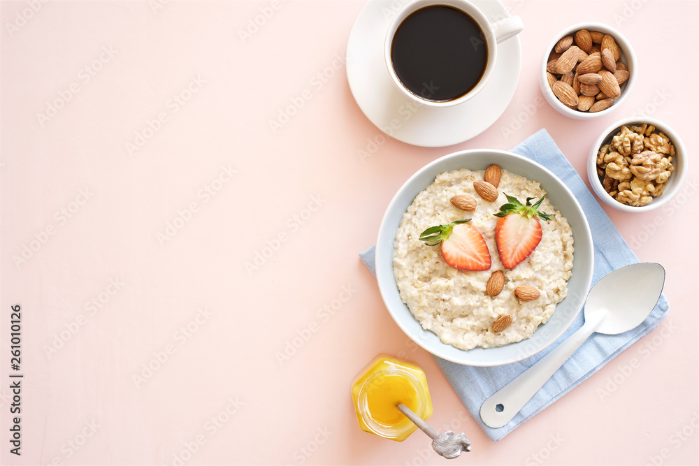 Oatmeal with honey, nuts and strawberries for breakfast. Light pink background. Flat lay