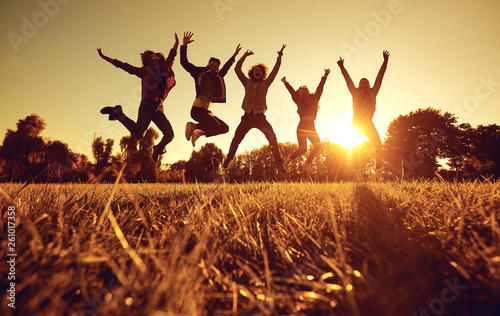 A group of young people jumping on the grass in the park at sunset. 