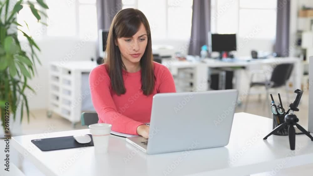 Young beautiful Caucasian businesswoman with brown hair sitting in office and using laptop. Young beautiful Caucasian businesswoman with brown hair sitting in office and using laptop.