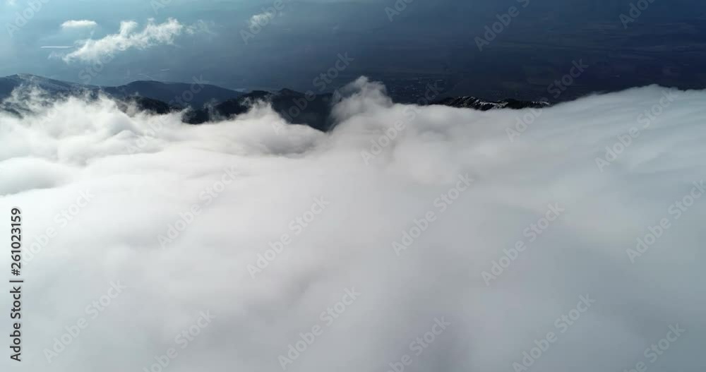 Aerial above the clouds over a mountain view and a small town behind Aerial above the clouds over a mountain view and a small town behind