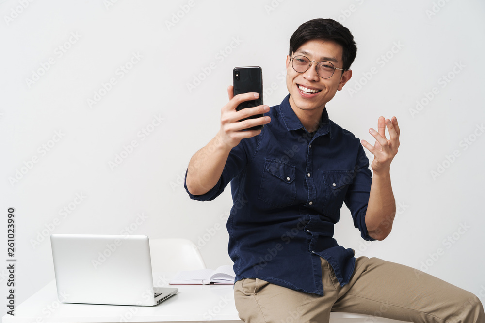 Φωτογραφία Photo of cheerful asian businessman sitting at table and holding smartphone whil
