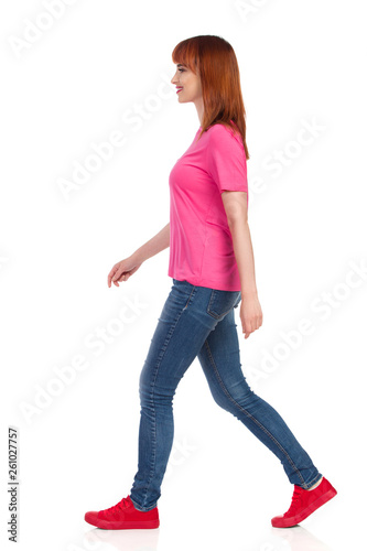 Side View Of Walking Beautiful Woman In Red Sneakers, Jeans And Pink Shirt