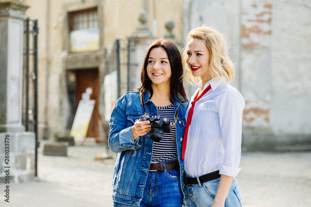 Outdoor lifestyle portrait of two best female friends traveler hipsters making photo on their vintage camera, having fun together, joy and happiness, wearing trendy bright clothes.