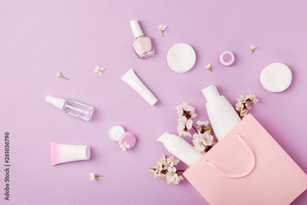 Set of woman's cosmetics in a bag with spring apricot bloom. Women's secrets. Spring female skin and hair care cosmetics in a bag on purple background. Cosmetic with apricot. Shampoo, lotion, tonic