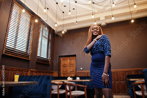 Portrait of beautiful young african business woman with dreadlocks, wear on blue blouse and skirt, posed in cafe.