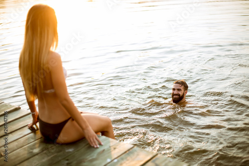 Young couple enjoying while woman sitting on pier and man swimming in the lake