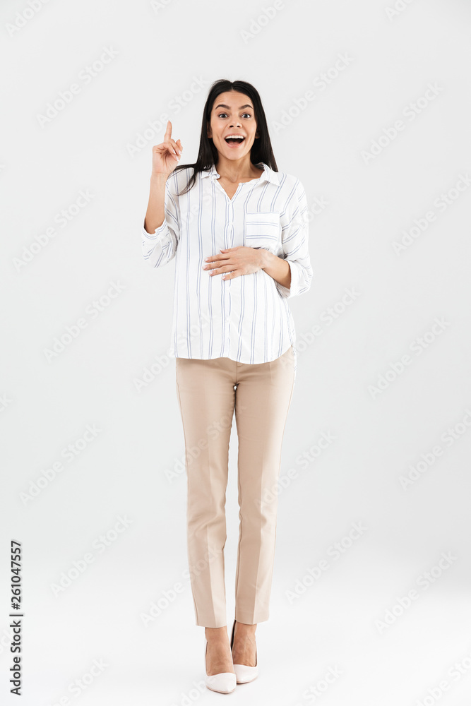 Full length photo of joyful pregnant businesswoman 30s smiling and touching her big tummy while standing Full length photo of joyful pregnant businesswoman 30s smiling and touching her big tummy while standing