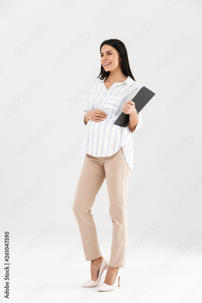 Full length photo of young pregnant businesswoman 30s holding clipboard and touching her big tummy Full length photo of young pregnant businesswoman 30s holding clipboard and touching her big tummy