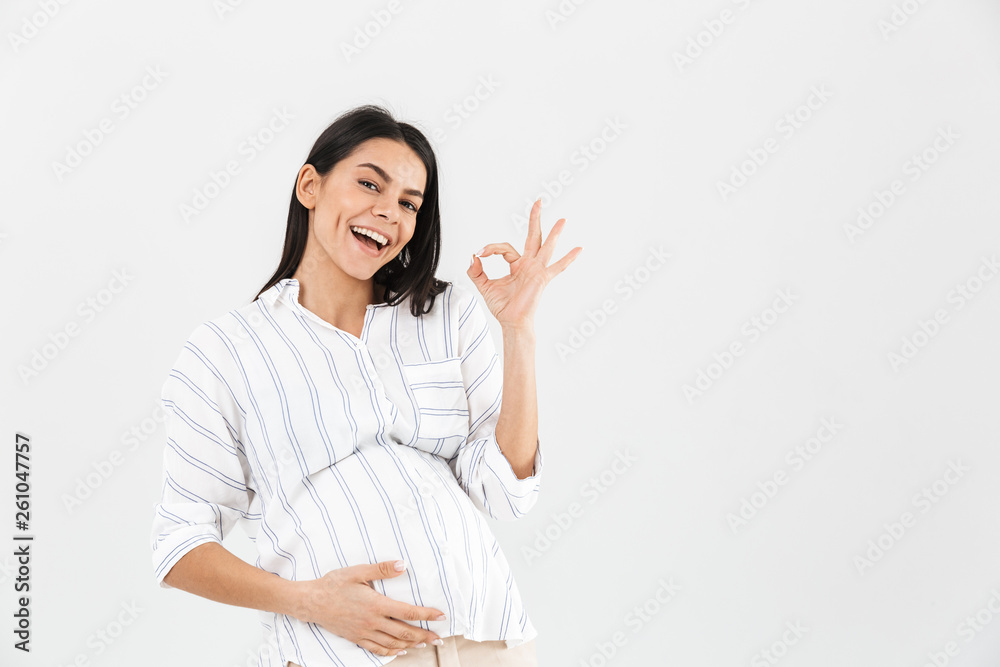 Photo of happy pregnant woman 30s with big belly smiling and showing ok sign Photo of happy pregnant woman 30s with big belly smiling and showing ok sign