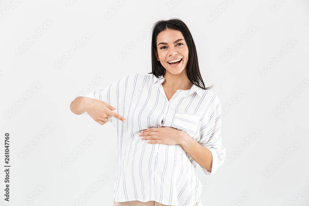 Photo of pleased pregnant woman 30s smiling and pointing fingers at her big belly Photo of pleased pregnant woman 30s smiling and pointing fingers at her big belly