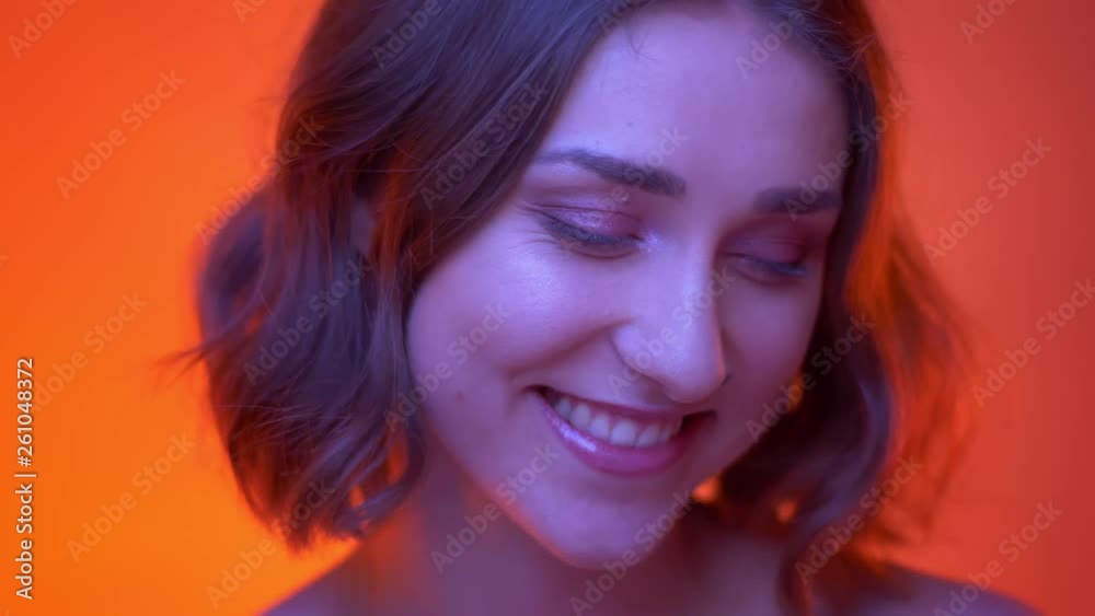 Closeup shoot of young attractive caucasian female smiling cheerfully looking at camera with neon red background Closeup shoot of young attractive caucasian female smiling cheerfully looking at camera with neon red background