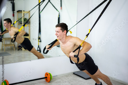 A young man is engaged in the gym on the TRX simulators in front of a mirror. Sport and a healthy body.