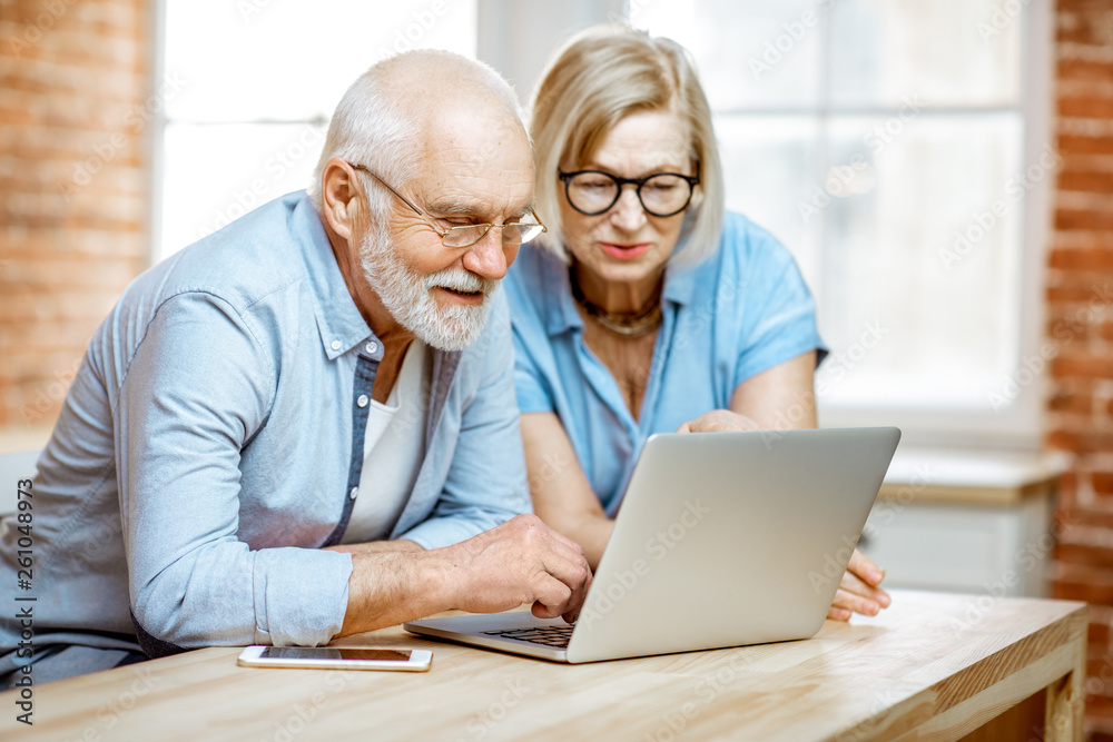 Portrait of a beautiful senior couple in blue shirts feeling happy, sitting together with laptop at home Portrait of a beautiful senior couple in blue shirts feeling happy, sitting together with laptop at home