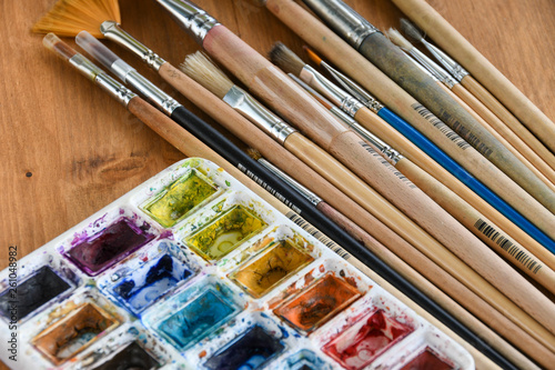 Colorful watercolor, acrylic paints and set of different brushes on wooden boards, closeup.