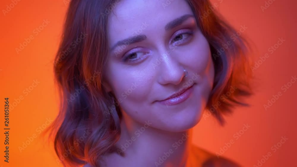 Closeup shoot of young attractive caucasian female turning to camera and smiling happily with neon red background Closeup shoot of young attractive caucasian female turning to camera and smiling happily with neon red background