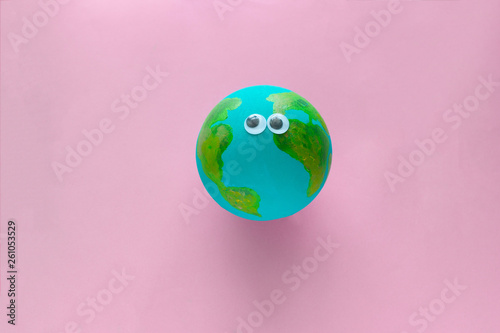 Earth planet model with googly eyes on a pastel pink background