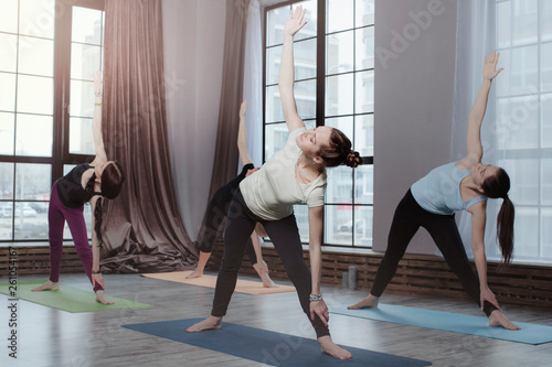 group of young women doing triangle pose yoga on yoga mat and relax breathing at studio.