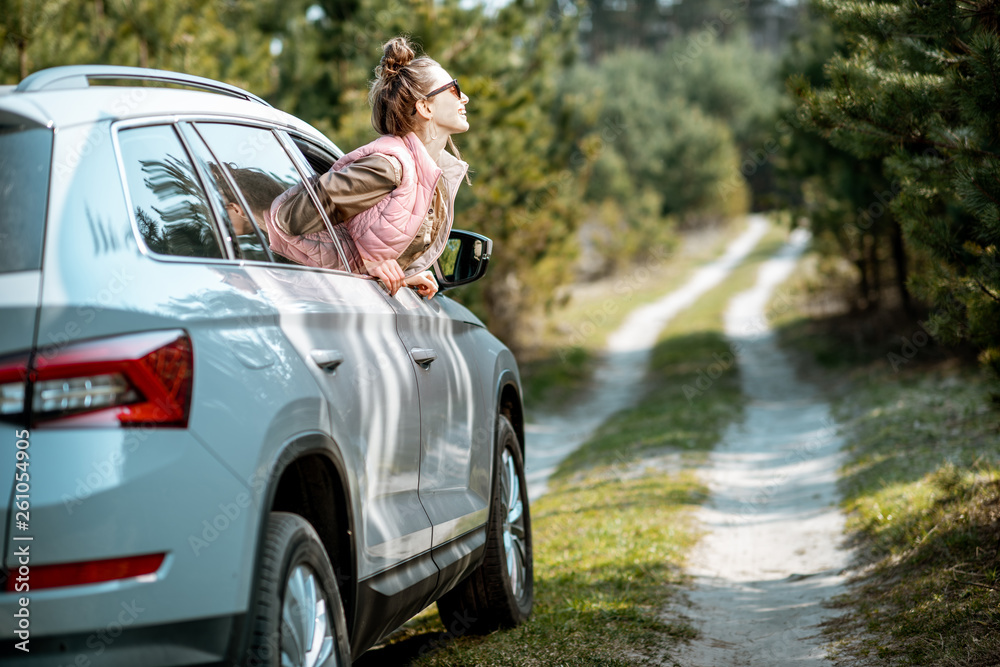 Young woman enjoying the trip, looking out the car window on a picturesque road in the woods Young woman enjoying the trip, looking out the car window on a picturesque road in the woods