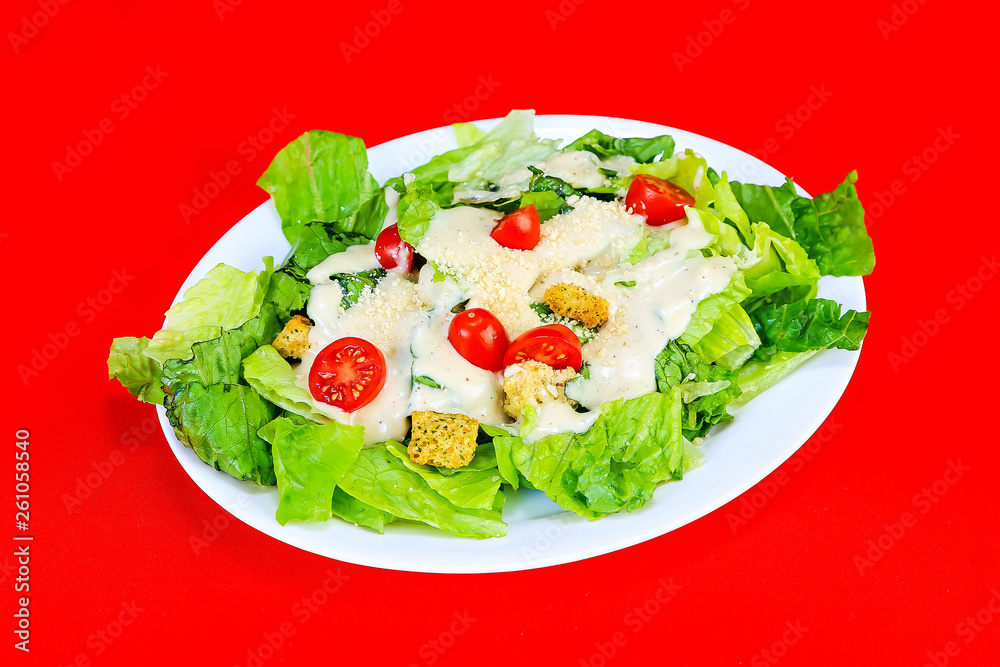 Sliced cherry tomatoes on Caesar Salad on white plate against red background. Sliced cherry tomatoes on Caesar Salad on white plate against red background.