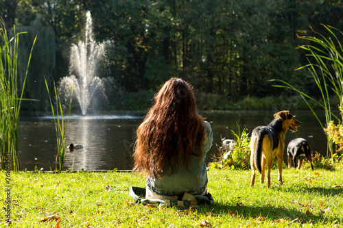 A girl relaxing in the grass at a pond with 2 dogs. photo