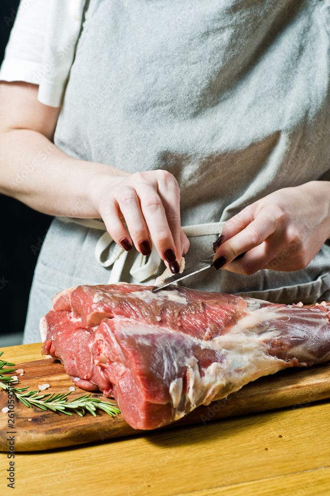 The chef cooking raw lamb leg on a wooden chopping Board. Rosemary, thyme, black pepper. Black background, side view, space for text