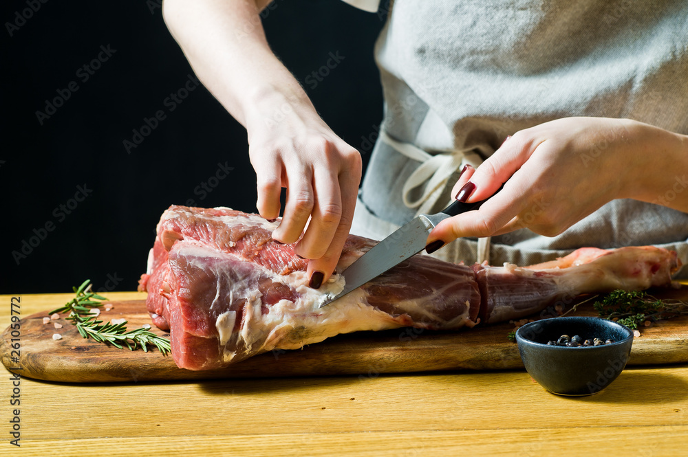 The chef cooking raw goat leg on a wooden chopping Board. Rosemary, thyme, black pepper. Black background, side view, space for text