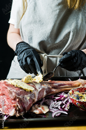 The chef marinates the raw leg of lamb. Black background, side view