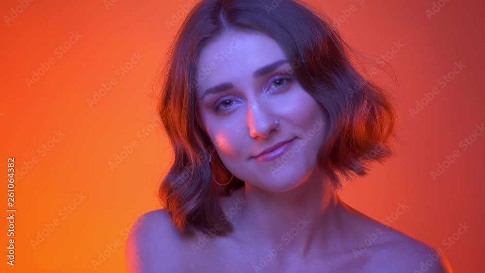 Closeup side view shoot of young attractive caucasian female with nose piercing posing in front of the camera with neon red background Closeup side view shoot of young attractive caucasian female with nose piercing posing in front of the camera with neon red background