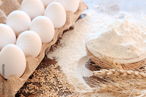 Wheat flour in a Cup on the table. Eggs and wooden objects of peasant life. Ingredients for making bread or baking.