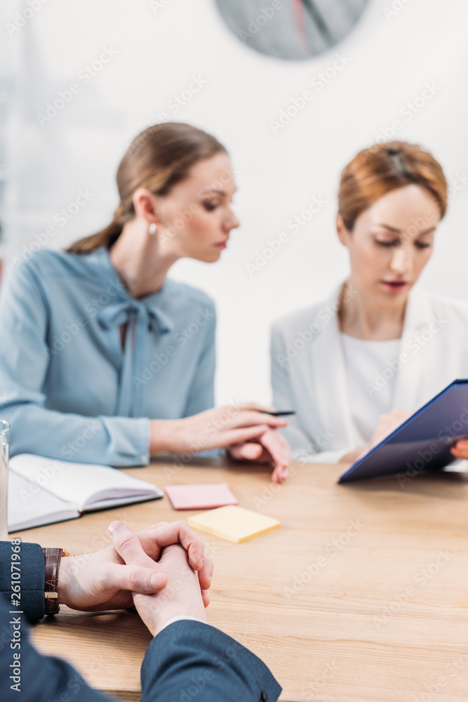 selective focus of man sitting with clenched hands near attractive recruiters selective focus of man sitting with clenched hands near attractive recruiters