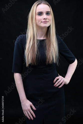 Studio portrait concept of a beautiful fashionable blond business girl standing and talking in a business dress on a black background.